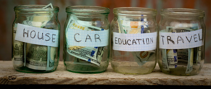 image of four jars with cash in it - one for house, one for car, one for education and one for travel - on a wooden shelf