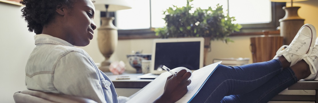 a woman with her feet up on a desk writing in a notebook