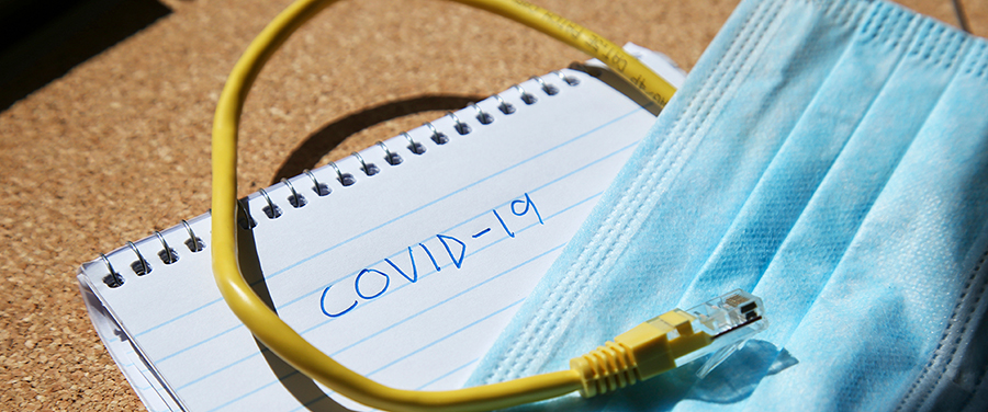 image of a note pad with covid-19 handwritten a mask and computer cable
