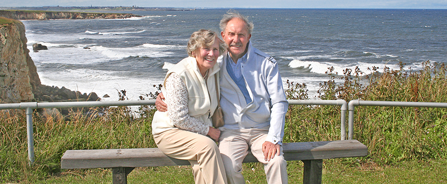 an image of an older couple sitting on a bench in front of the ocean