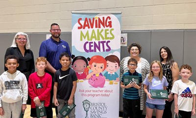 elementary school students and Bank staff around a Saving Makes Cents banner